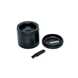 A black metal grinder with "ACHE GRYND" on the rim, a lid with a scoop, and a brush.