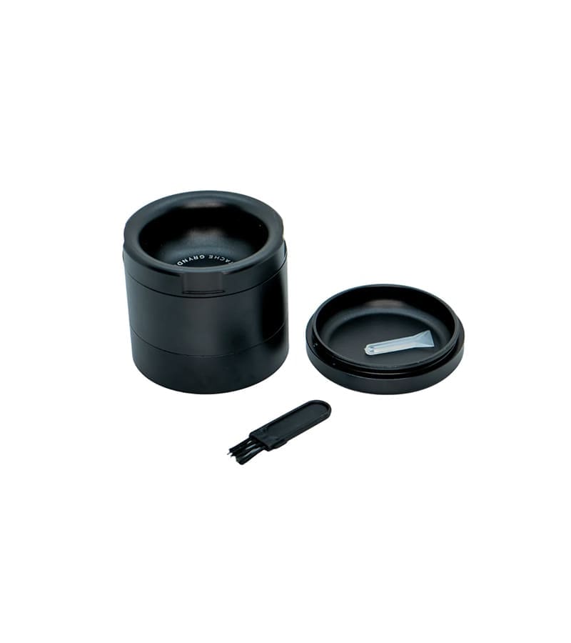 A black metal grinder with "ACHE GRYND" on the rim, a lid with a scoop, and a brush.