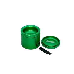 A shiny green herb grinder with its lid off, a small white scraper, and a black brush on a white background.