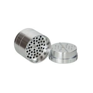 A silver metal grinder is open, showing a perforated bottom and a top with many small spikes.