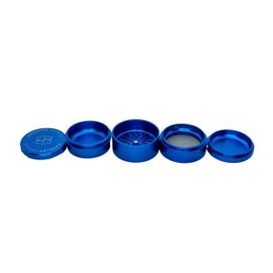 A four-piece blue metal herb grinder is disassembled, revealing "STACHE GRYNDER" on the lid.