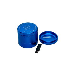 A blue "STACHE GRYNDER" with a small brush and a lid containing a white scoop on a white background.