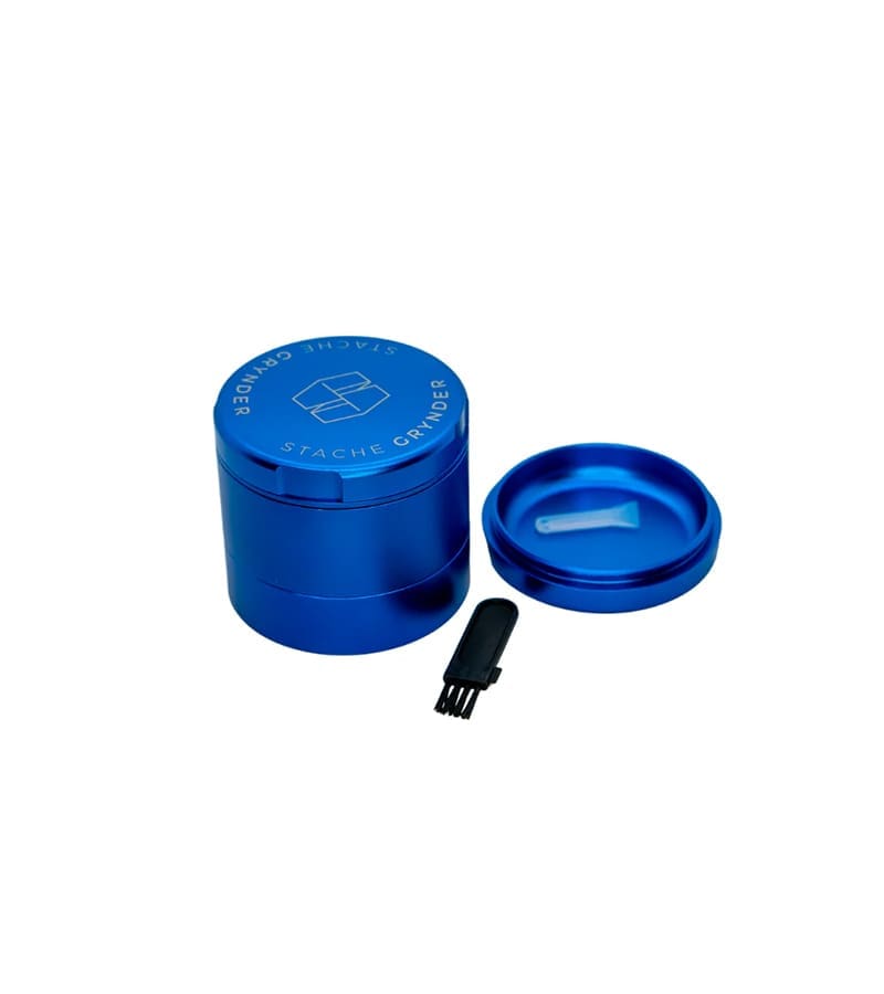 A blue "STACHE GRYNDER" with a small brush and a lid containing a white scoop on a white background.
