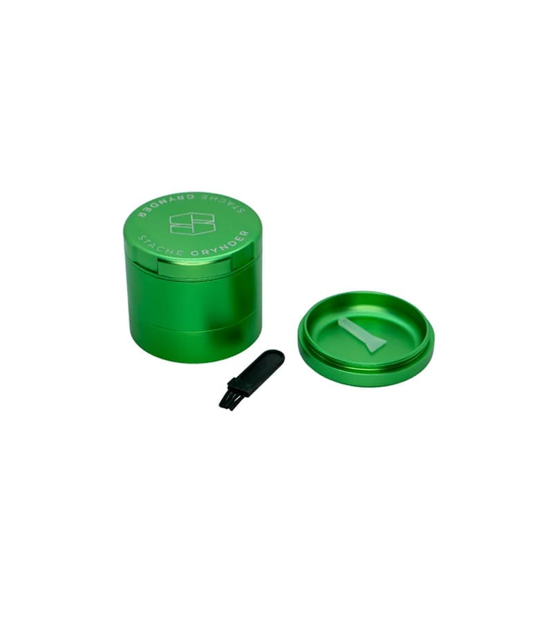 A metallic green "STACHE GRYNDER" with a logo on top, a small brush, and an open lid with a scraper.