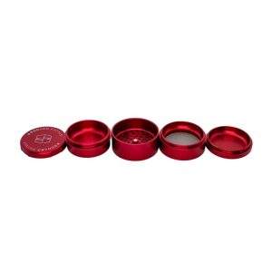 A disassembled red metal grinder with four parts laid out horizontally, revealing "STACHE GRYNDER" on the cap.