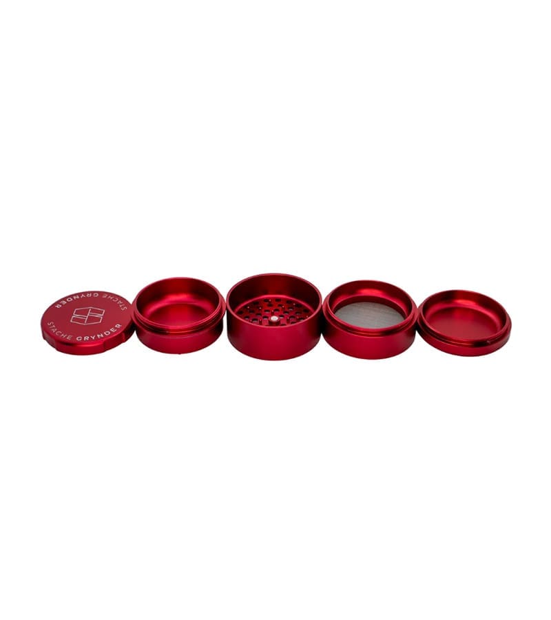 A disassembled red metal grinder with four parts laid out horizontally, revealing "STACHE GRYNDER" on the cap.