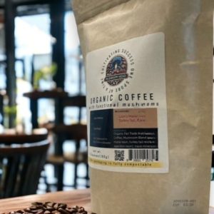 A bag of "ORGANIC COFFEE with functional mushrooms" sits on a pile of coffee beans in a cafe.