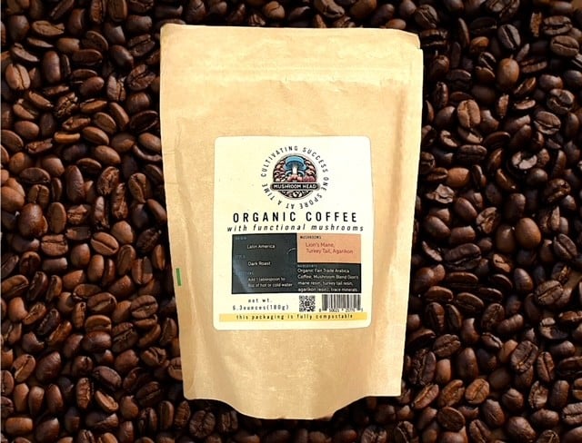 A light brown bag of "ORGANIC COFFEE with functional mushrooms" sits on a bed of dark roasted coffee beans.