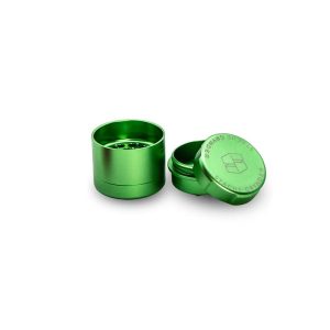 A bright green metal grinder with its top removed, displaying "GRYNDER" and "STACHE" text.
